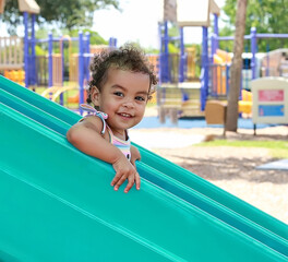 Young girl with curly hair has fun as she goes down a playground slide at a local park. 