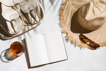 Summer holiday concept. Travel flat lay with notepad, backpack, and hat on white table background.
