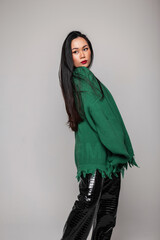 Fashion beauty model woman with red lips in green stylish ripped sweater poses in studio. Pretty asian girl