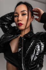 Fototapeta na wymiar Fashionable studio portrait of a beautiful young Asian woman with red lips wearing a fashionable snakeskin leather jacket and bra posing in the studio and looking at the camera