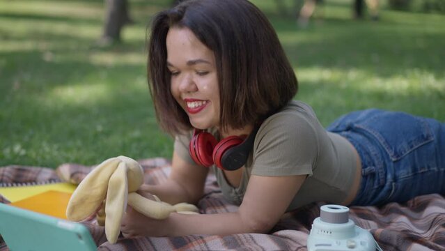 Relaxed positive little woman playing with toy lying on blanket in spring summer park. Portrait of joyful happy Caucasian person with dwarfism enjoying leisure outdoors. Slow motion