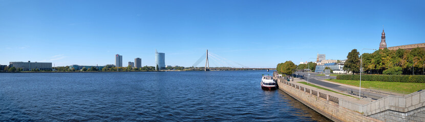 Fototapeta na wymiar Panoramic view of the Baltic Capital of Riga Latvia. Embankment, view of the riverside with tourist ship and modern skyscrapers. Sunny day in Summer.