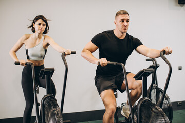 Fototapeta na wymiar Young man and woman using air bike for cardio workout at cross training gym