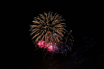 Firework over the ordinary European city at night near water, orange, pink, red.