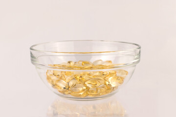 Close up omega 3 (fish oil) capsules in a glass bowl on a white glossy table	