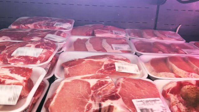 Raw sliced meat in plastic containers wrapped in cling film stands on the shelves of the refrigerator in the supermarket