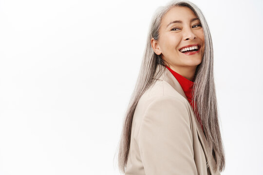 Portrait of healthy and happy asian senior woman, middle aged korean lady with long grey hair, laughing and smiling, white perfect teeth, studio background