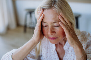 Portrait of an attractive senior woman sitting on a sofa at home with a headache
