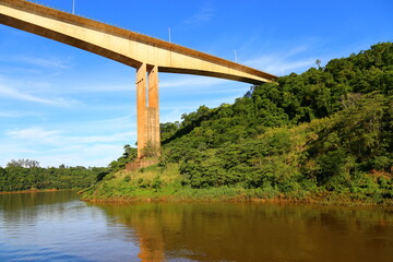 Fototapeta na wymiar Bridge over the Iguacu river connecting Brazil and Argentina. Tall column under the bridge, water of the river and green vegetation.