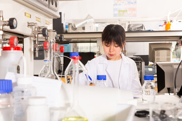 Nice Chinese female student noting results of research at chemical lab