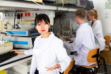 Portrait of young Chinese woman scientist engaged in research in chemical laboratory with her colleagues