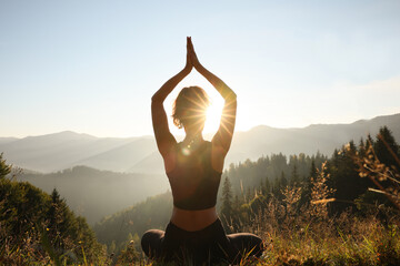 Woman practicing yoga in mountains at sunrise, back view