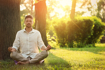 Naklejka na ściany i meble Man meditating in park on sunny morning. Practicing yoga