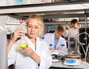 Attractive female student performing experiments in university laboratory, examining chemical substances in glass lab flask