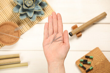 Naklejka premium Woman holding many acupuncture needles over white wooden table, top view