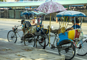 Fototapeta na wymiar Cycling tricycles - traditional rickshaws stand on the street next to the sidewalk