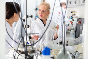 Focused young woman lab technician with her Chinese female assistant working with reagents in test...