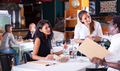 Obraz premium smiling female waiter taking order from adult man and woman in restaurante