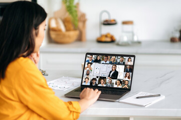 Online learning, professional development. Asian girl, sits at home, listening to a webinar using a video conference, on the screen a group of multiracial people gathered for a brainstorm or lecture