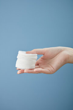 Front view of hand model holding cotton pad in blue background for cosmetic advertising
