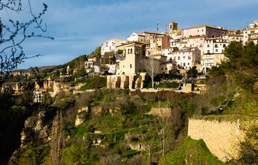 Fototapeta na wymiar Scenic view of Cuenca cityscape on rocky ledge overlooking oldest Catholic parish church of San Miguel on sunny spring day, Spain..