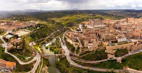 Picturesque aerial view of Toledo cityscape on green hilly banks of Tagus river in early spring overlooking fortified Alcazar castle framed by four towers, Spain
