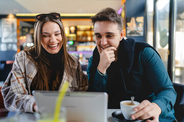 Two people young adult couple woman and man boyfriend and girlfriend or wife and husband sitting at cafe relationship concept use digital tablet for online search or video call real people copy space