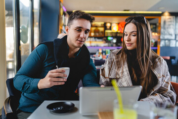 Two people young adult couple woman and man boyfriend and girlfriend or wife and husband sitting at cafe relationship concept use digital tablet for online search or video call real people copy space