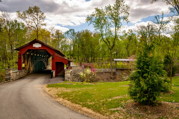 Fototapeta na wymiar View of a Restored Burr Truss Covered Bridge on a Country Road With Stone Approach Walls on a Mostly Sunny Day