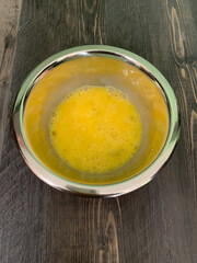 Three beaten eggs in a stainless steel bowl.