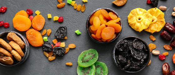 Bowls with different dried fruits on dark background, top view