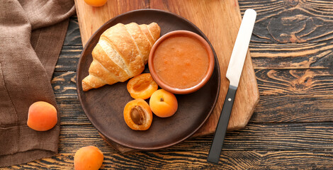 Plate with tasty apricot jam and croissant on wooden table, top view