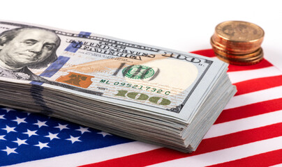 A stack of 100 American dollars bills and coins on the background of a fragment of the American flag