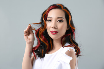 Young Asian woman with beautiful colorful hair on grey background