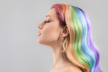 Pretty young woman with rainbow hair on grey background