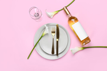 Beautiful table setting with calla lilies and bottle of wine on pink background