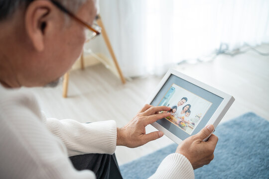 Asian senior male sitting alone on sofa and looks family photographs.
