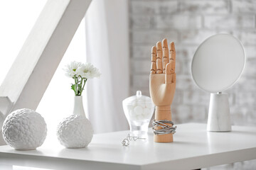 Wooden hand with bracelet and flowers in vase on table in room