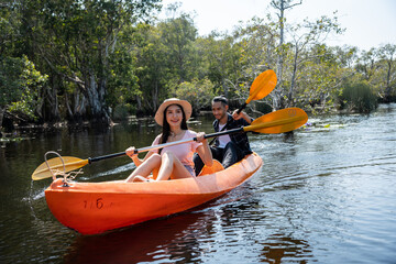 Asian attractive romantic young couple rowing kayak in a forest lake.	