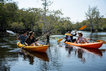 Group of Asian young man and woman play rowing kayak in a forest lake.