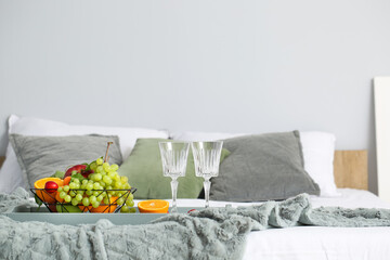 Tray with fruit basket and empty glasses on bed