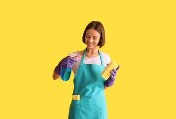 Young woman with cleaning sponge and bottle of detergent on yellow background