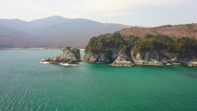 A beautiful rocky island and a cape in a beautiful bay covered with coniferous trees. Sea waves crash on the shore. Beautiful rocks are covered with pine trees. The concept of outdoor recreation