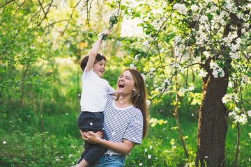 Fototapeta premium Mother with little baby son in spring garden during golden hour. Mom and son are active in nature. Family walks in a spring garden. Happy mother's day