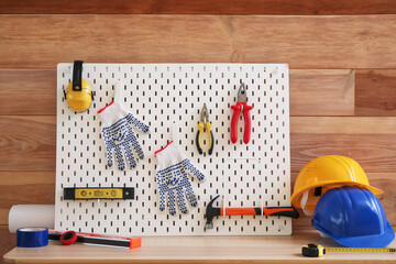 Pegboard with modern tools on desk near wooden wall in workshop