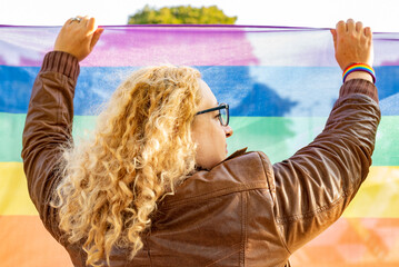 Back view or a lesbian activist holding a LGBT rainbow flag. Concept of Pride. Pride month. 