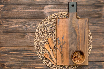Cutting board, bowl with nuts and spoons on wooden background