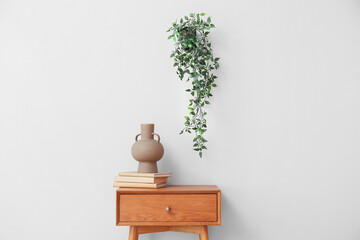 Vase with books on wooden table near light wall