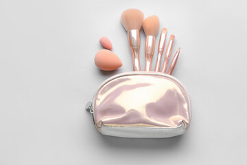 Set of makeup brushes with sponges and bag on light background