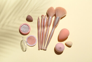 Makeup brushes with sponges and cosmetics on color background